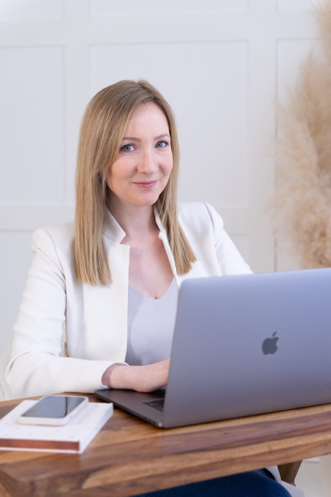 Csilla webdizájner fehér blézerben a laptopja mellett mosolyog – brand fotózás szentendrei fotóstúdióban