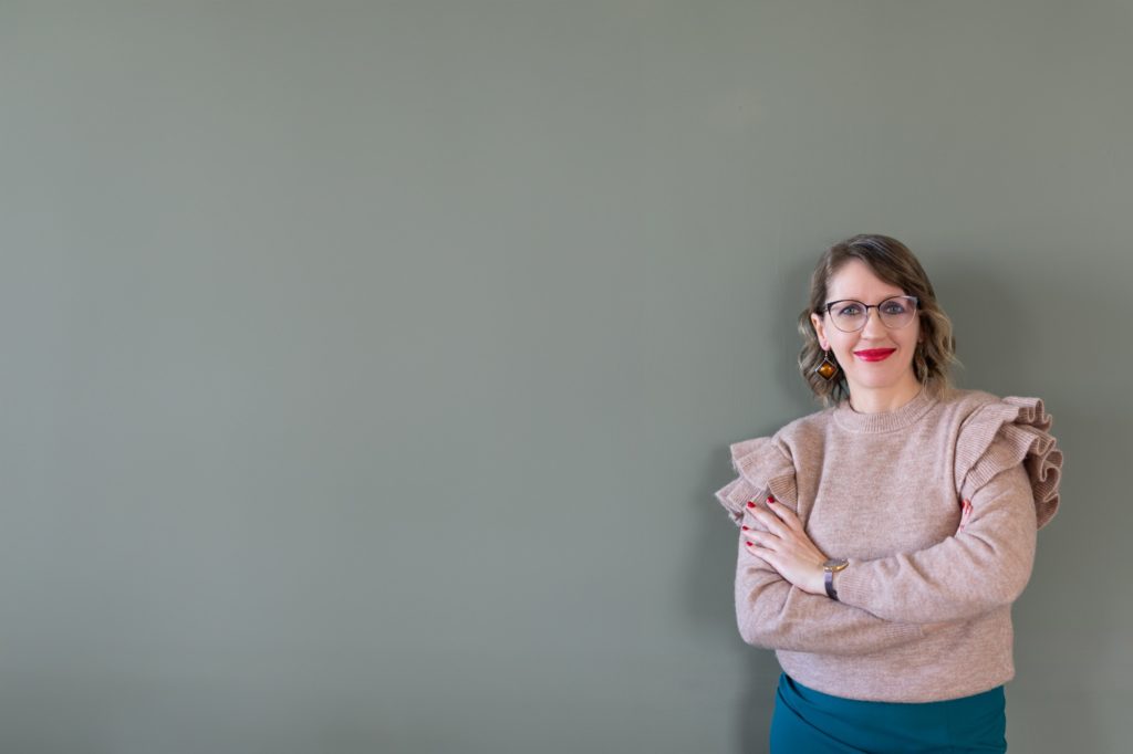 Júlia virtuális asszisztens karba tett kézzel egy zöld fal előtt
