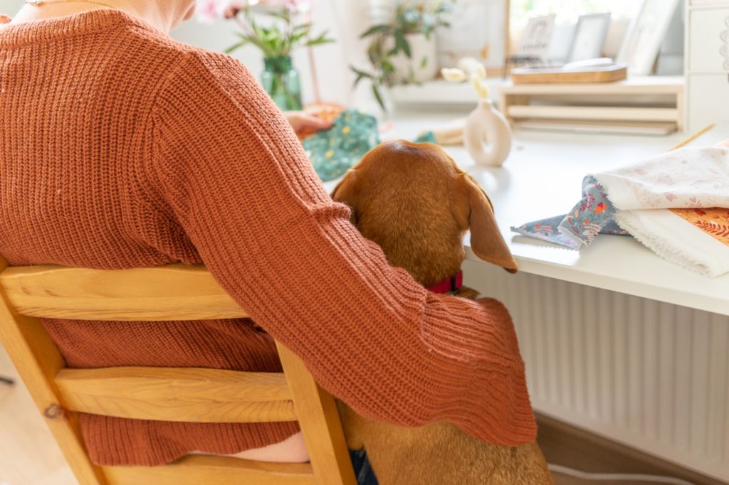 Termékkészítő vállalkozónő a munkaasztalánál dolgozik, mellette egy kutya