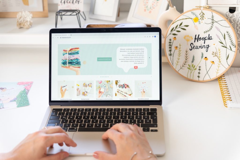 Laptop a munkaasztalon, a képernyőn egy webshop, mellette hímzőráma