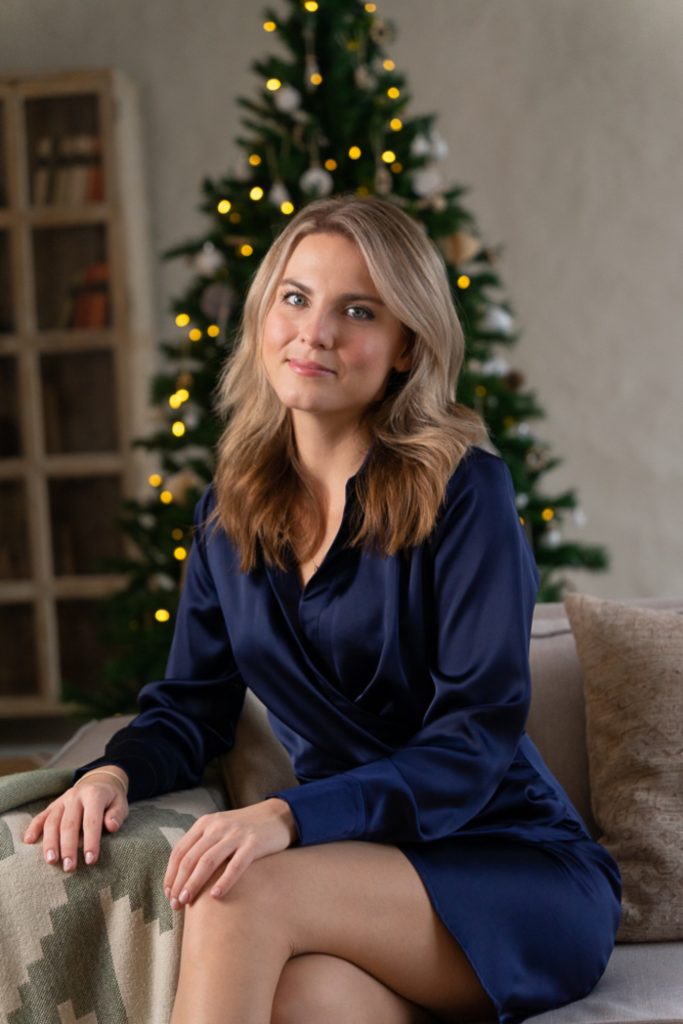 Vállalkozónő sötétkék ruhában ül, mögötte karácsonyfa