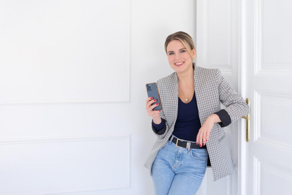 Vállalkozónő kockás blézerben, telefonnal a kezében egy ajtónak dől – business fotózás