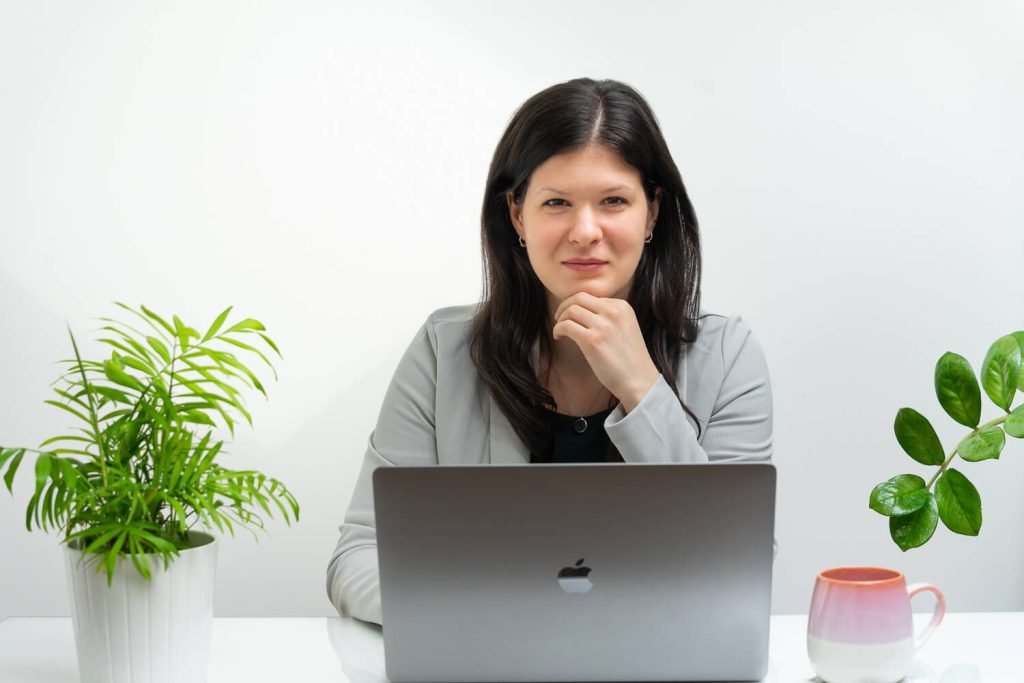 Fekete hajú vállalkozónő mosolyog a laptopja mögött, kezét az álla alá téve