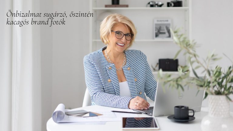 Szőke, szemüveges vállalkozónő kockás blézerben mosolyog a laptopja előtt